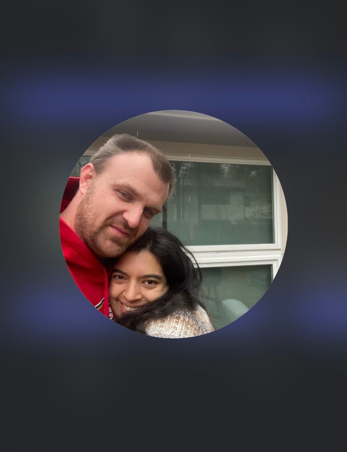Smiling woman with long dark hair leaning against a man in a red hoodie.
