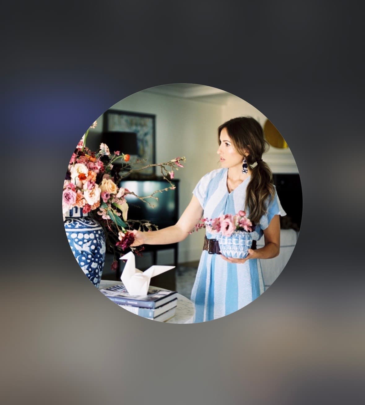 Woman in blue striped dress arranging pink flowers in blue and white patterned vases.