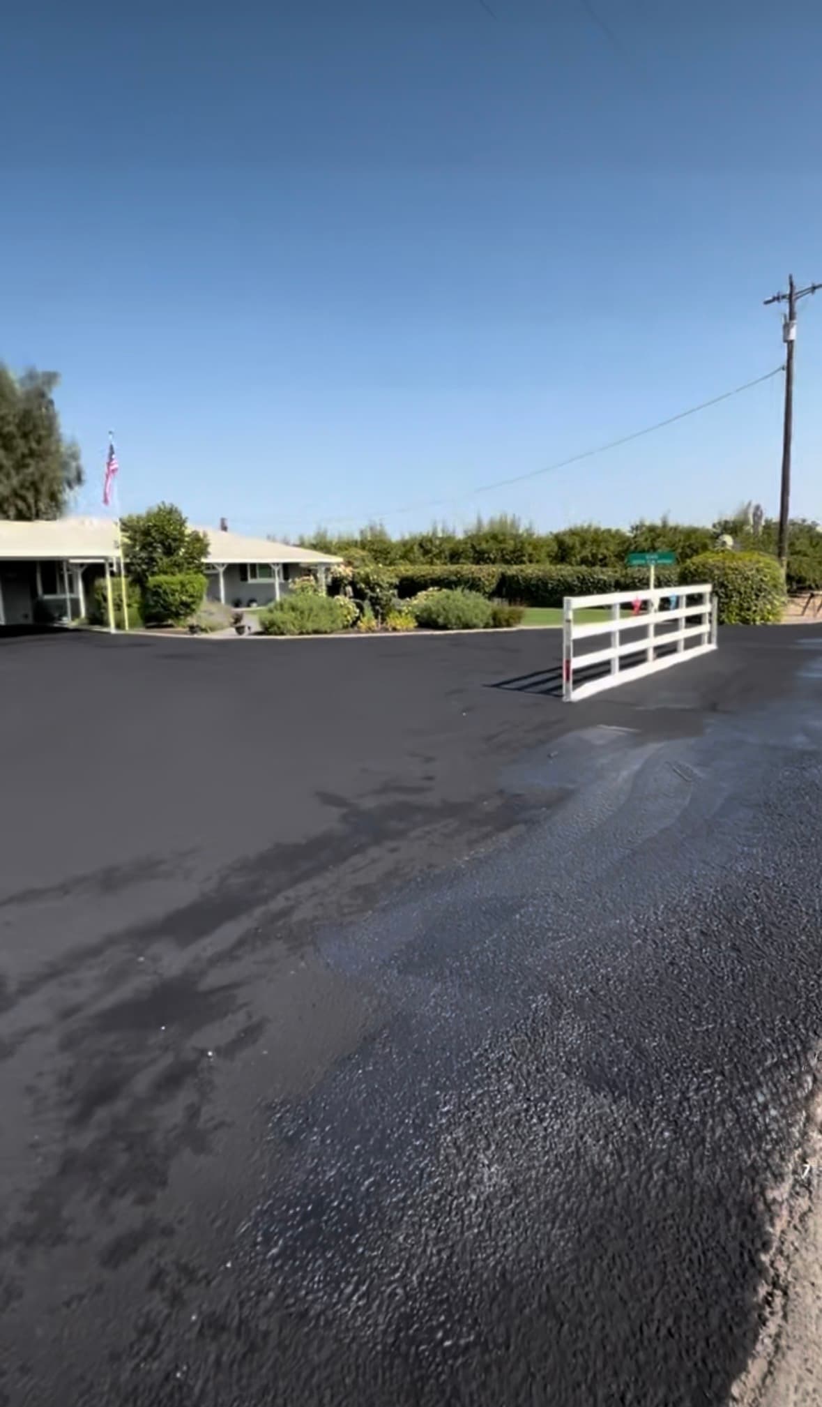 Freshly sealed black asphalt driveway in front of a house with a white fence.