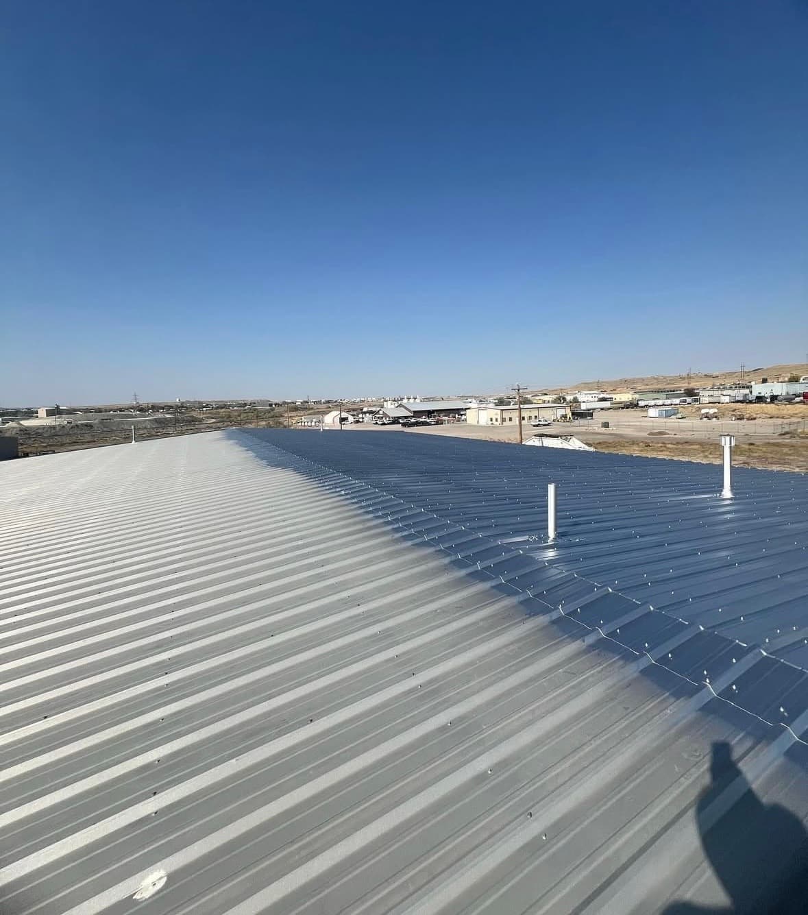 Corrugated metal roof partially coated with blue sealant under a clear blue sky.