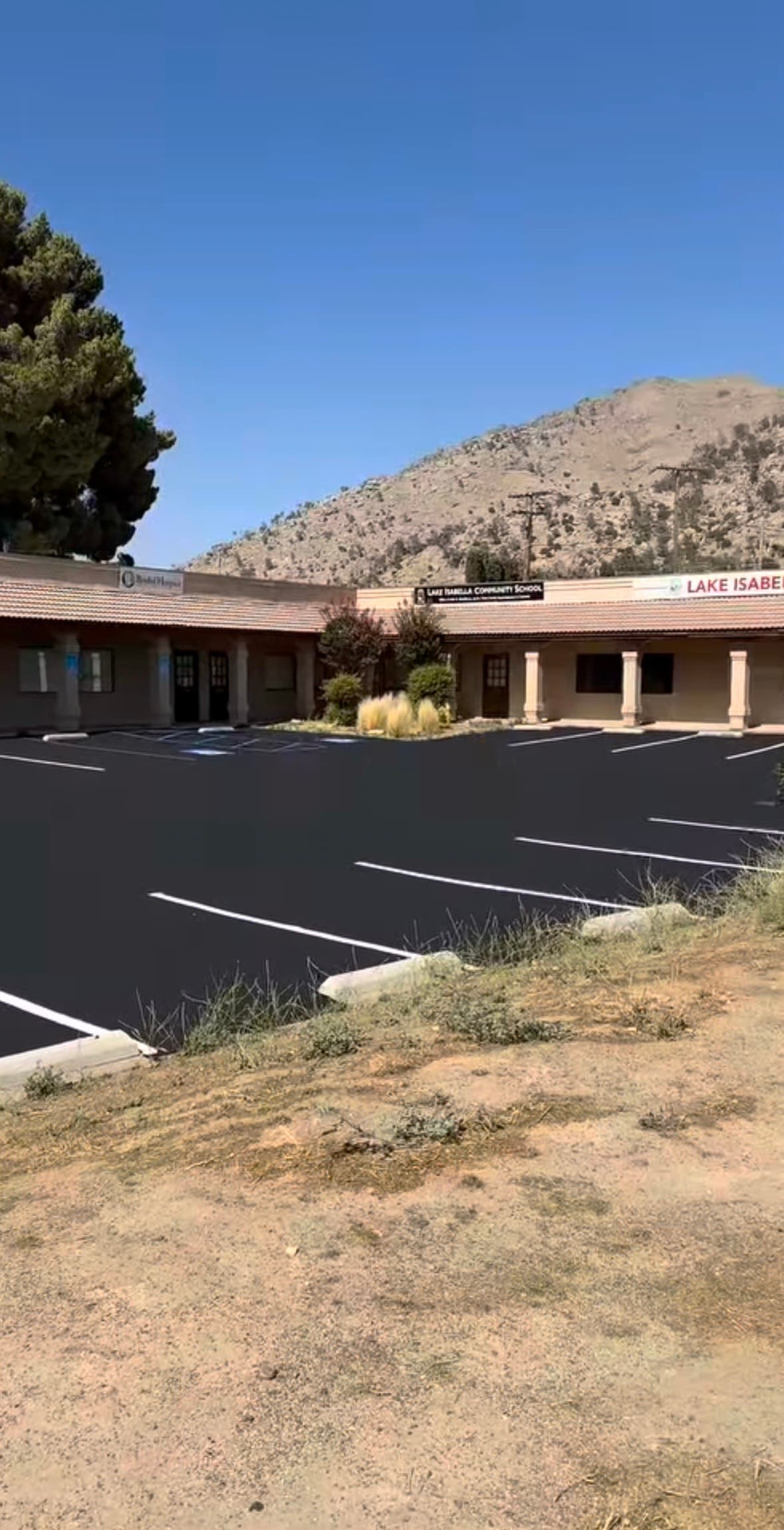 Freshly paved black asphalt parking lot at Lake Isabella Community School with mountains behind.