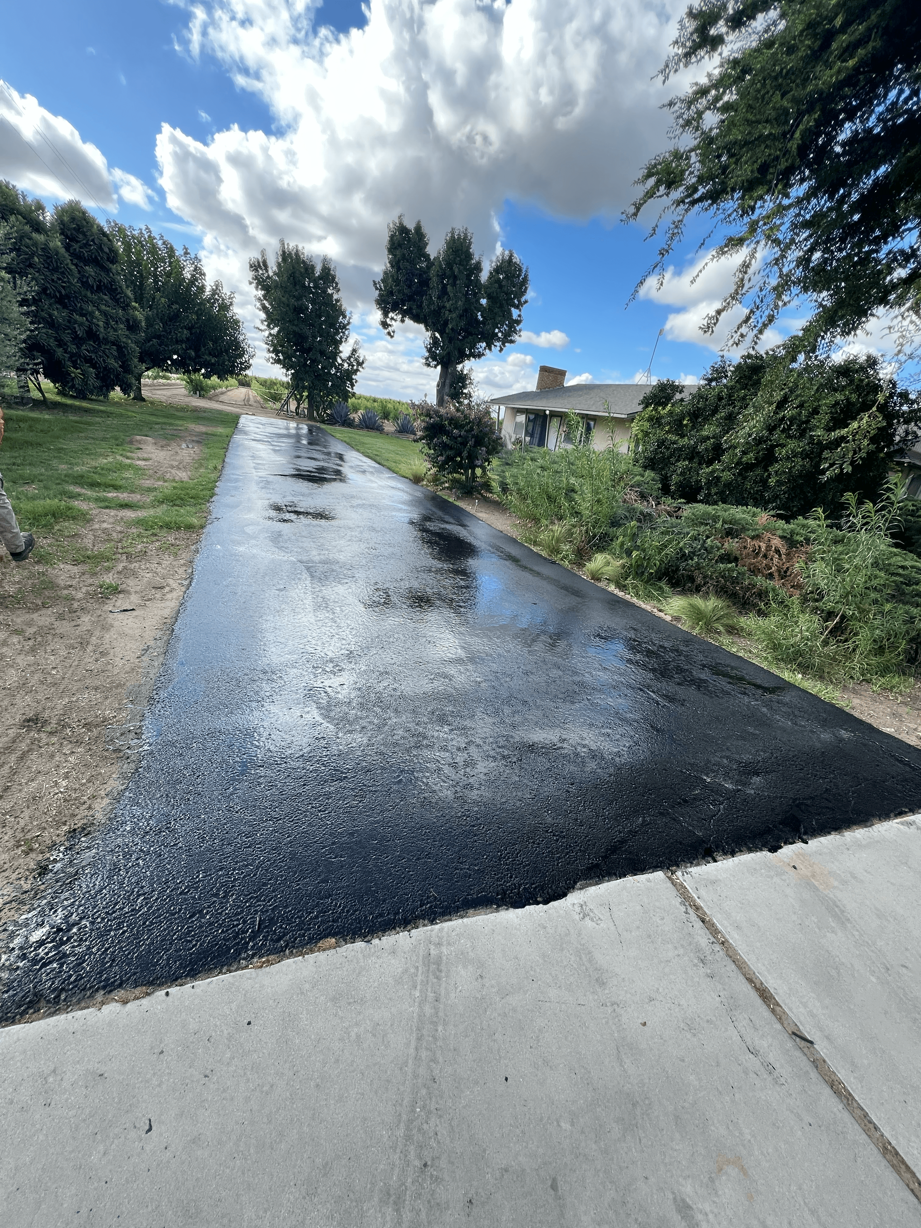 Freshly sealed black asphalt driveway reflecting the blue sky and clouds on a sunny day.
